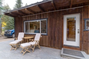Een houten chalet met een veranda, een eethoek met stoelen en een tafel, en een voertuig dat ervoor geparkeerd staat.