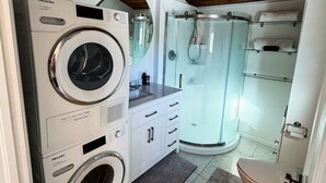 A compact laundry room with a front-loading washing machine, a dryer, and a glass-enclosed shower.
