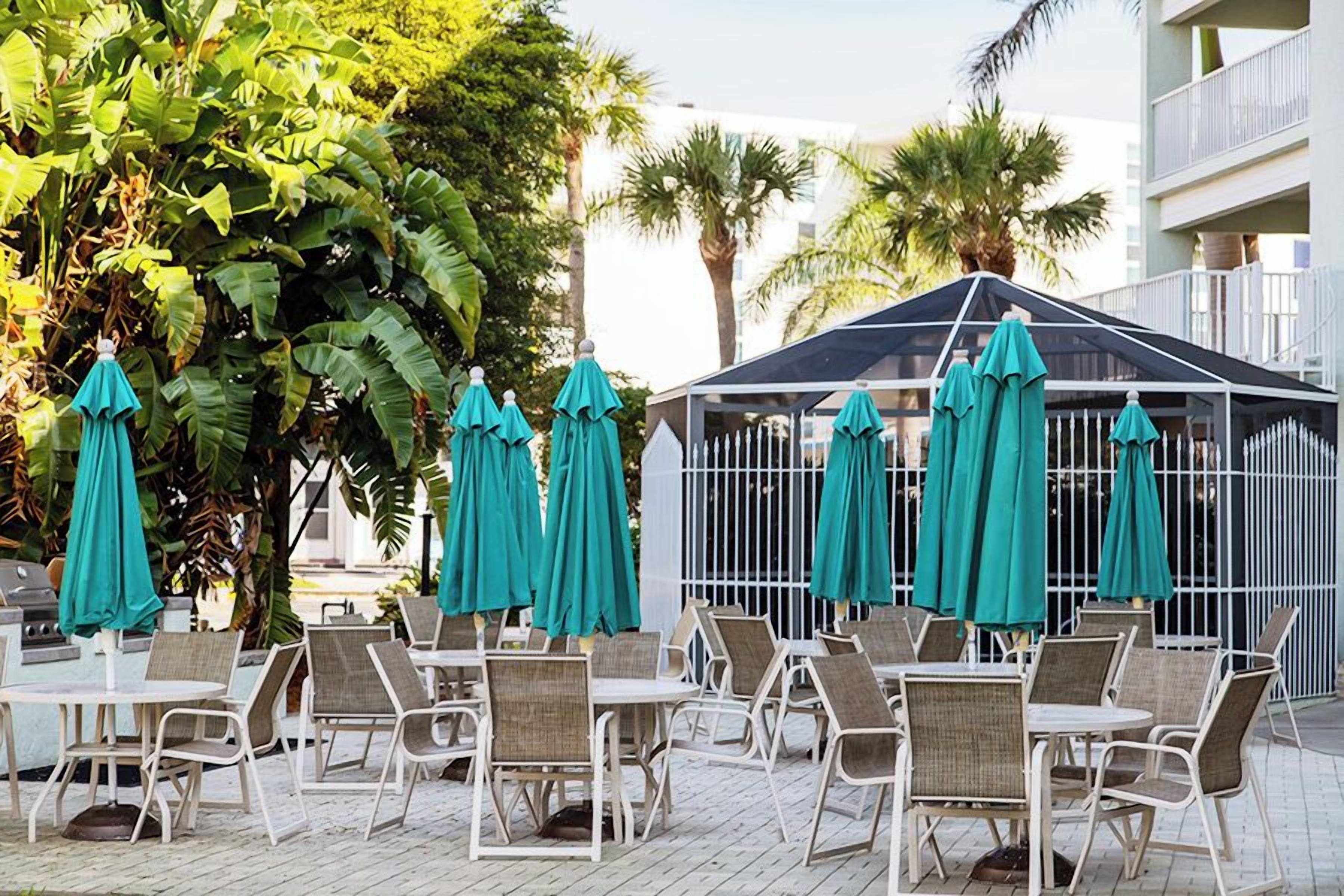 Outdoor seating with tables and chairs, some covered by umbrellas, and a fenced area with a roof.