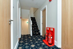 A hallway with a carpeted floor, a fire extinguisher mounted on the wall, and a staircase in the background. - Contractor-Friendly 6BR 6 En-Suites | Free Parking (Kent)