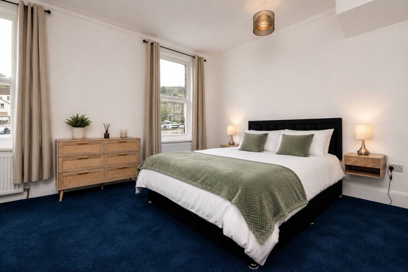 A bedroom with a large bed, a dresser, a nightstand, and a window with curtains.