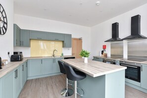 Eine moderne Küche mit hellblauen Schränken, einer Holz Arbeitsplatte, einer zentralen Kochinsel mit einem schwarzen Stuhl und Edelstahlgeräten.