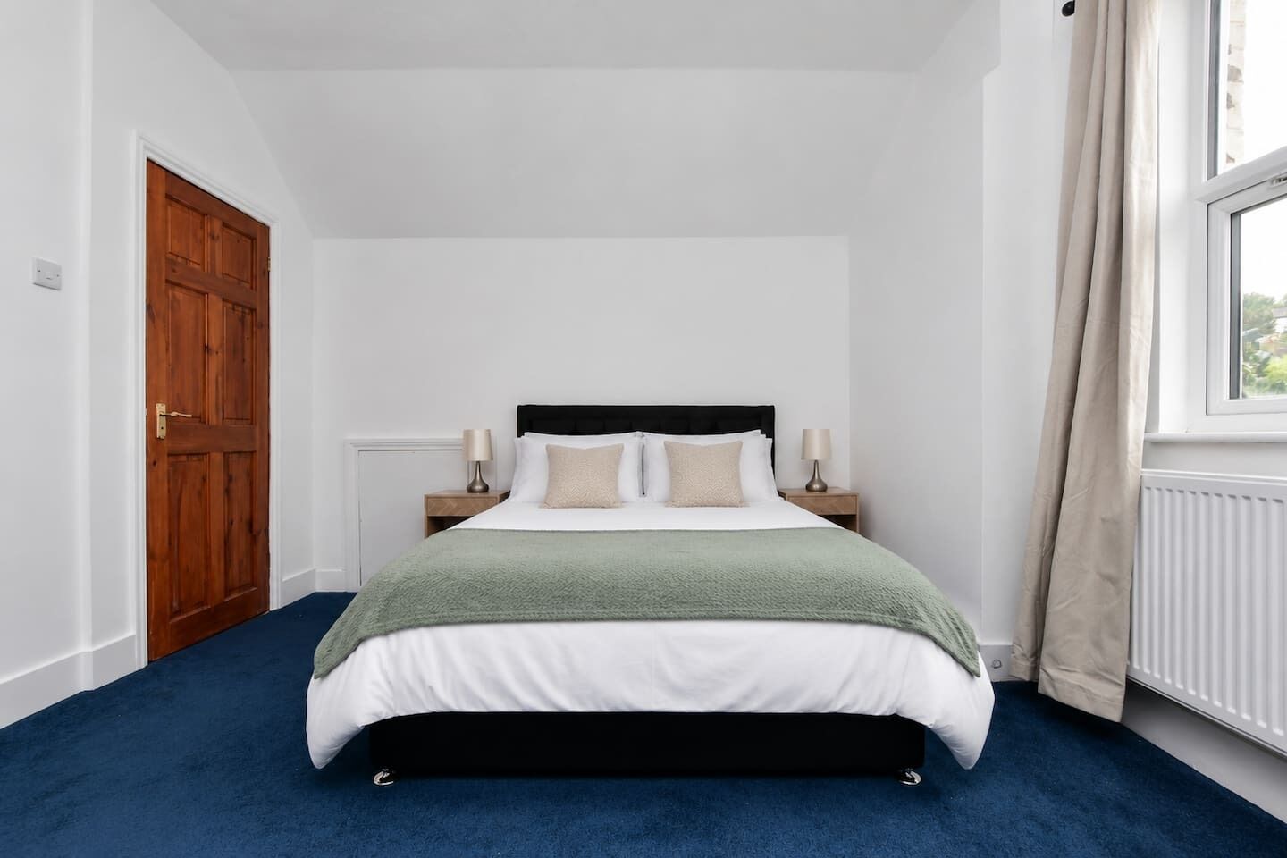 Une chambre à coucher avec un lit, deux tables de chevet, une fenêtre avec des rideaux et une porte.