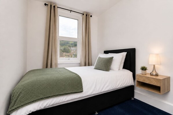 A bedroom with a bed, a nightstand, a lamp, and a window with curtains.