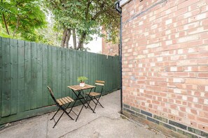 Eine Terrasse mit Tisch und Stühlen, ein grüner Zaun und eine Ziegelwand.