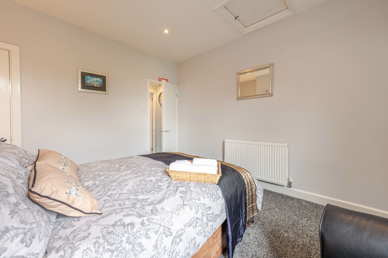 A bedroom with a bed, a bedside table, a mirror, and a door.