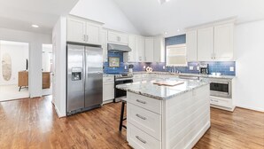 Eine moderne Küche mit weißen Schränken, einem Edelstahl-Kühlschrank, einem eingebauten Backofen und einer großen Kochinsel mit Marmorarbeitsplatte.
