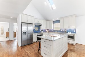 A modern kitchen with white cabinets, a stainless steel refrigerator, a built-in oven, and a large island with a marble countertop. - 2 Min. Walk to Beach/Ocean Views/Hot Tub/Game Room/Bikes/In-Law Suite (St. Augustine)