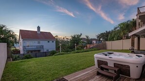Ein Garten mit Whirlpool, Holzterrasse und einem Haus.