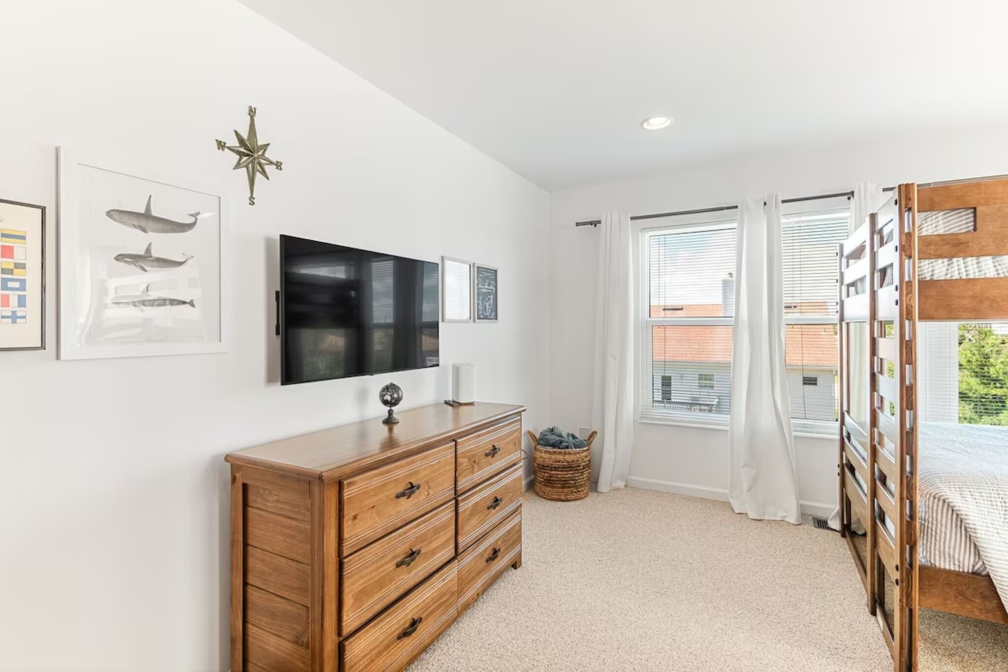 Un dormitorio con un aparador de madera, un televisor de pantalla plana, una brújula en la pared y una cama litera.