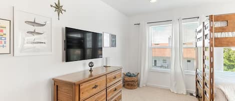 Une chambre à coucher avec une commode en bois, un téléviseur à écran plat, une boussole fixée au mur et un lit superposé.