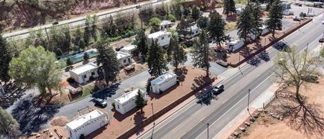 An aerial view of a campground with RVs parked along a road, surrounded by trees and a dirt path.