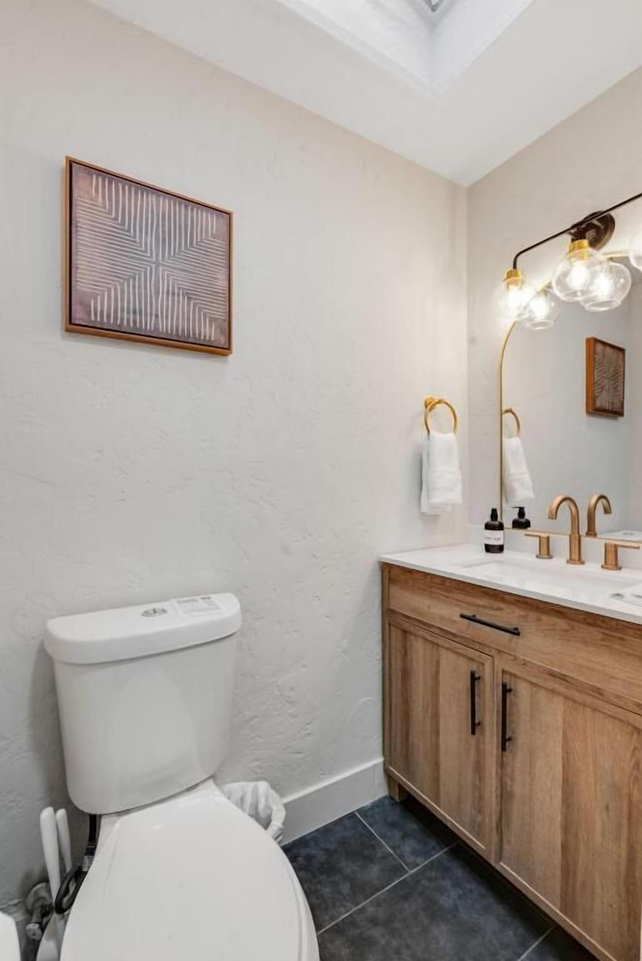 A bathroom with a toilet, wooden cabinet, and a wall-mounted light fixture.
