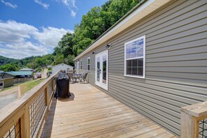 A deck with outdoor furniture, a grill, and a view of a green landscape.