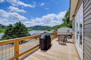 Une terrasse en bois dotée d’un barbecue couvert, d’une table et de chaises, et offrant une vue sur un lac et des montagnes.