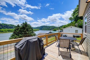 Une terrasse avec une table et des chaises, offrant une vue sur un lac et des collines boisées.