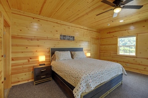 Ein Schlafzimmer einer Holzhütte mit einem Bett, Nachttischen, einem Deckenventilator und einem Fenster.