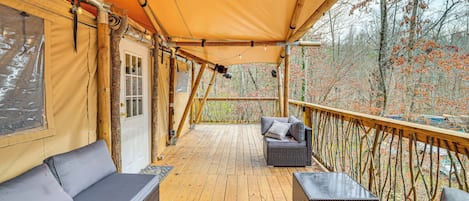 Een overdekt houten terras met rieten meubilair, uitzicht op bomen en een houten balustrade.