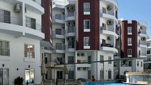 A multi-story residential building with balconies, a swimming pool, and a clear sky. - Modern Pool-View Studio with Gym, Pool Pub & Restaurant in Aqua Palms Resort (Hurghada)