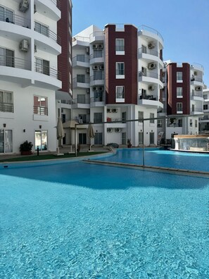 A multi-story residential building with balconies, a swimming pool, and a clear sky. - Modern Pool-View Studio with Gym, Pool Pub & Restaurant in Aqua Palms Resort (Hurghada)