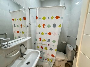 A bathroom with a shower curtain featuring colorful fish and sea creatures, a sink with a faucet, and a toilet. - Modern Pool-View Studio with Gym, Pool Pub & Restaurant in Aqua Palms Resort (Hurghada)