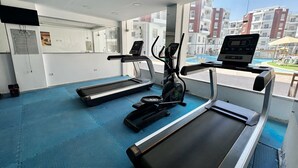 A gym with treadmills, an elliptical, and a rowing machine, with a view of a swimming pool and buildings outside. - Modern Pool-View Studio with Gym, Pool Pub & Restaurant in Aqua Palms Resort (Hurghada)