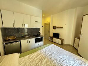 A compact hotel room with a kitchenette, a bed, a television, and a wardrobe. - Modern Pool-View Studio with Gym, Pool Pub & Restaurant in Aqua Palms Resort (Hurghada)