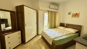 A hotel room with a bed, a wardrobe, a desk, and an air conditioning unit. - Modern Pool-View Studio with Gym, Pool Pub & Restaurant in Aqua Palms Resort (Hurghada)