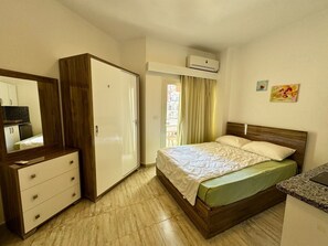 A hotel room with a bed, a wardrobe, a desk, and an air conditioning unit. - Modern Pool-View Studio with Gym, Pool Pub & Restaurant in Aqua Palms Resort (Hurghada)