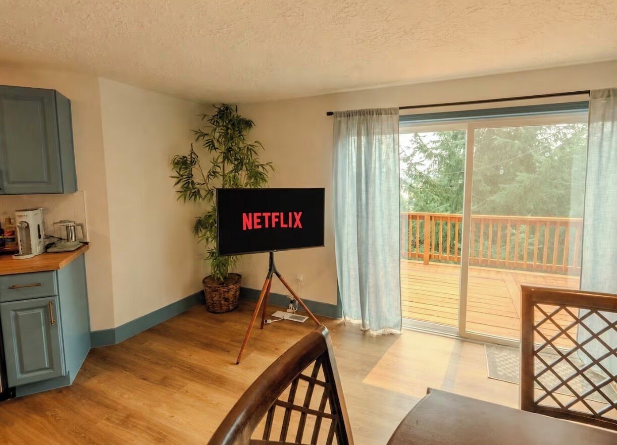 Ein Zimmer mit Fernseher auf einem Schrank, einem Esstisch, einer Küchenzeile und einer Glasschiebetür zu einer Terrasse.