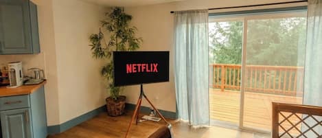 Ein Zimmer mit Fernseher auf einem Schrank, einem Esstisch, einer Küchenzeile und einer Glasschiebetür zu einer Terrasse.