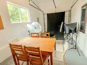 Ein Zimmer mit Holztisch und -stühlen, einem Fenster sowie Fotoausrüstung.
