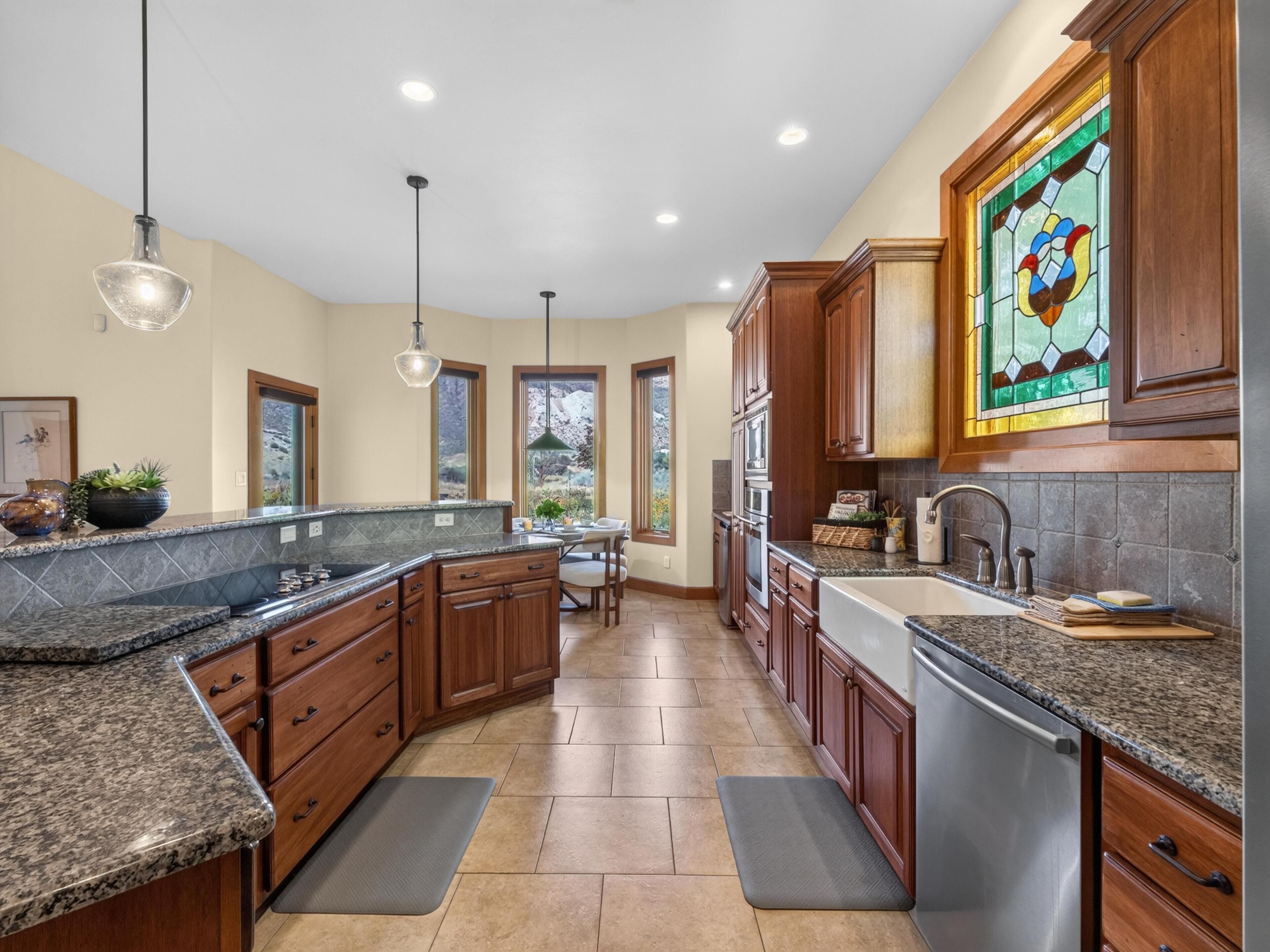 A spacious kitchen with granite countertops, wooden cabinets, and a large window.