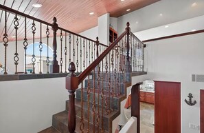 Una escala de fusta amb barana de metall ornamentada, que condueix a una zona d'estar amb cuina.