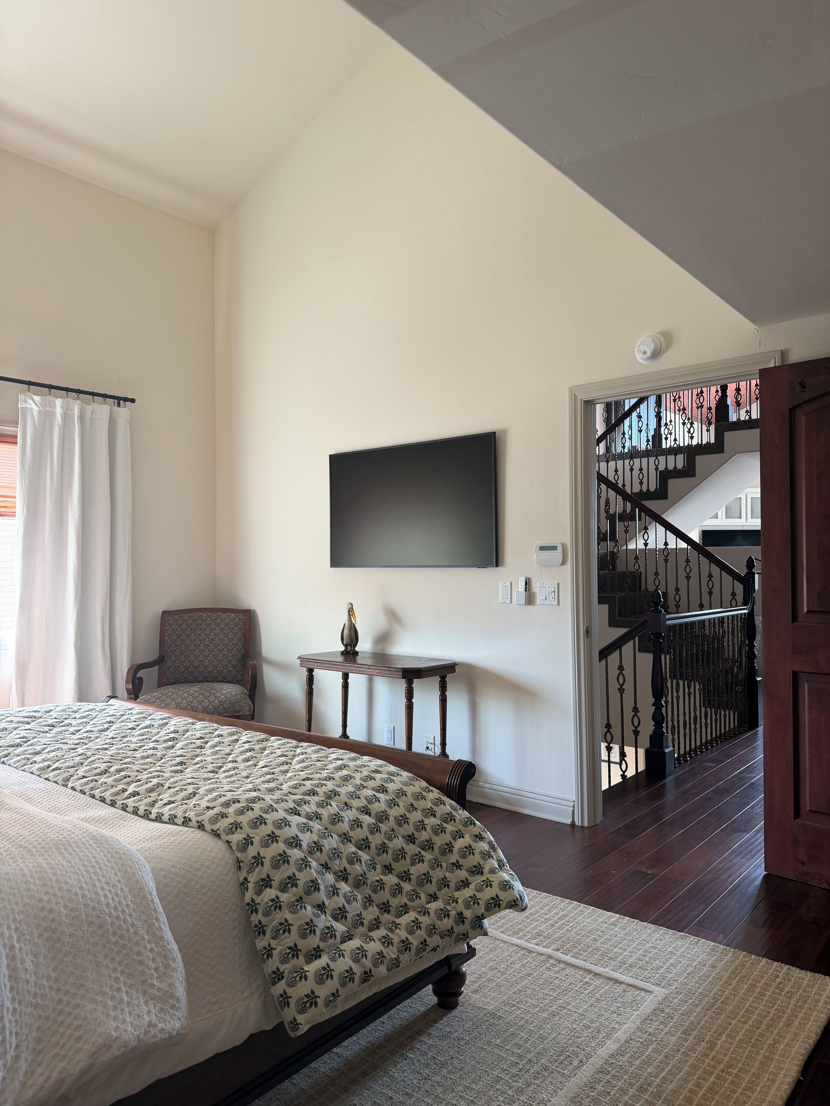 Une chambre à coucher comprenant un lit, une chaise, une petite table, un téléviseur à écran plat et un escalier menant à un autre niveau.
