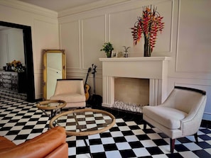 Una habitación con suelo a cuadros, una chimenea, dos sillones, un espejo y una guitarra.