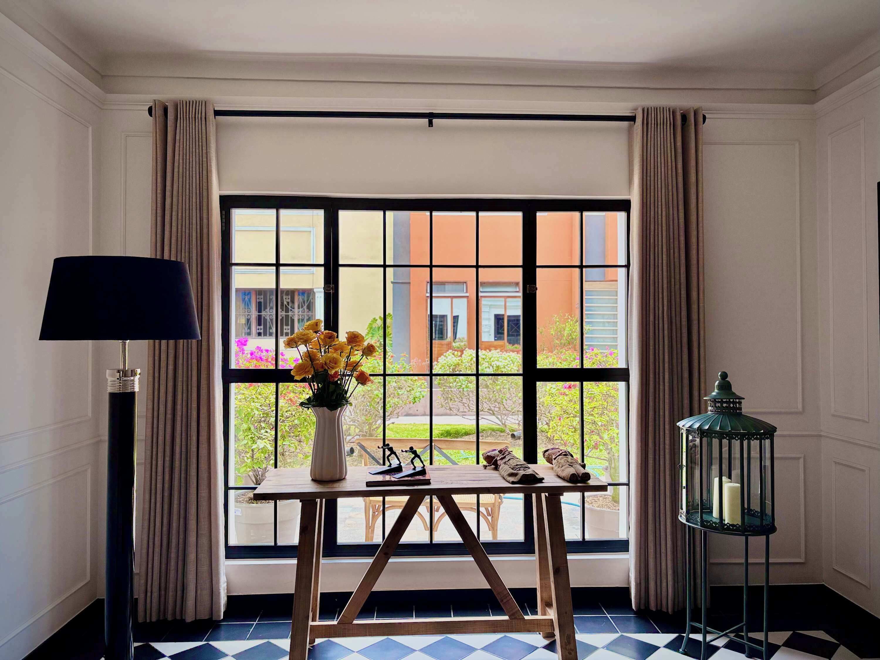 A room with a large window, a table with a vase of flowers, a lamp, and a lantern.