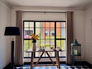 Una habitación con un ventanal grande, una mesa con un florero, una lámpara y un farol.