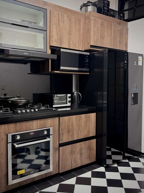 Una cocina moderna con armarios de madera, microondas, refrigerador negro, estufa y piso a cuadros.
