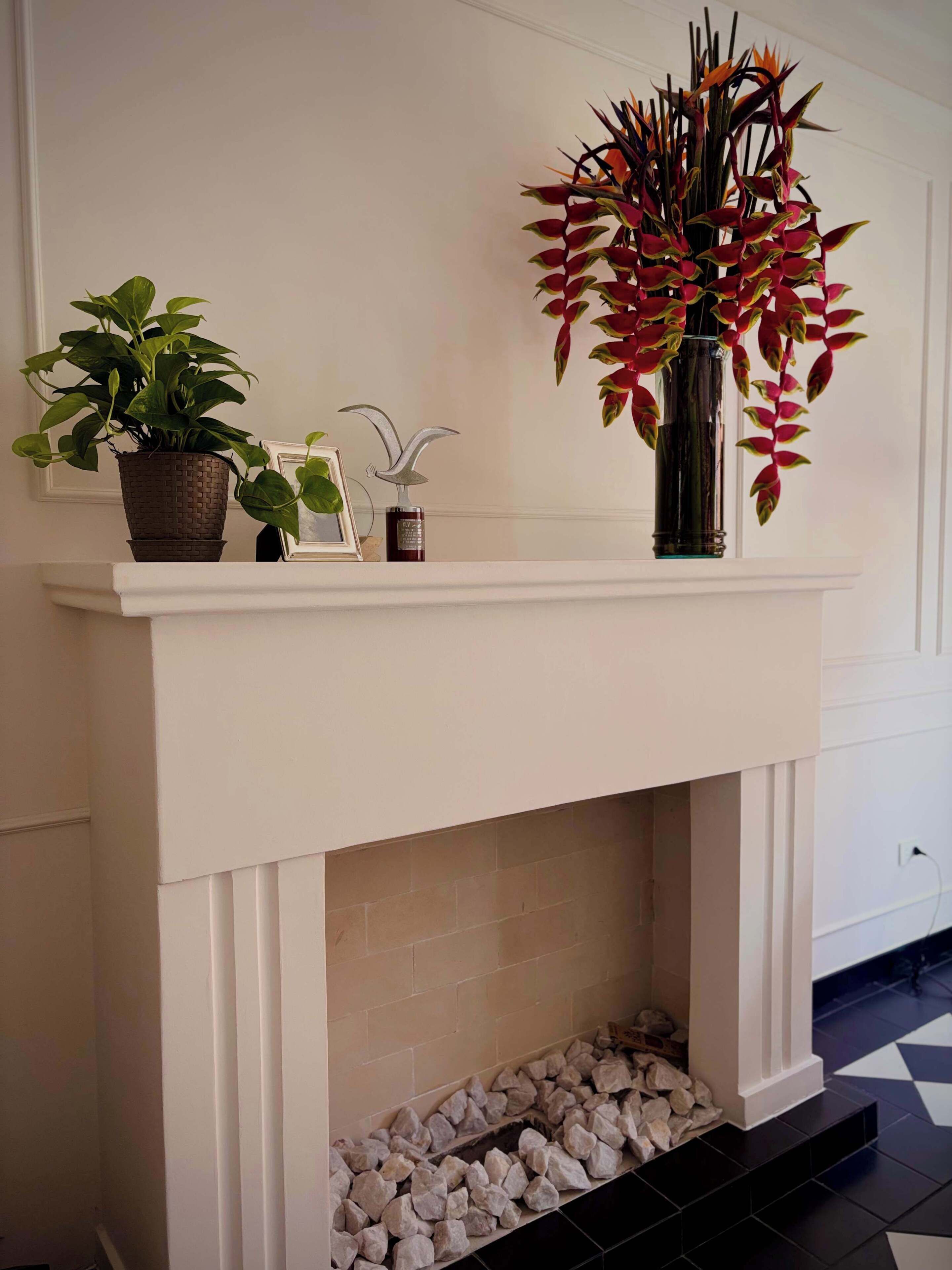 A fireplace mantel with a potted plant, a framed picture, and a decorative bird sculpture.