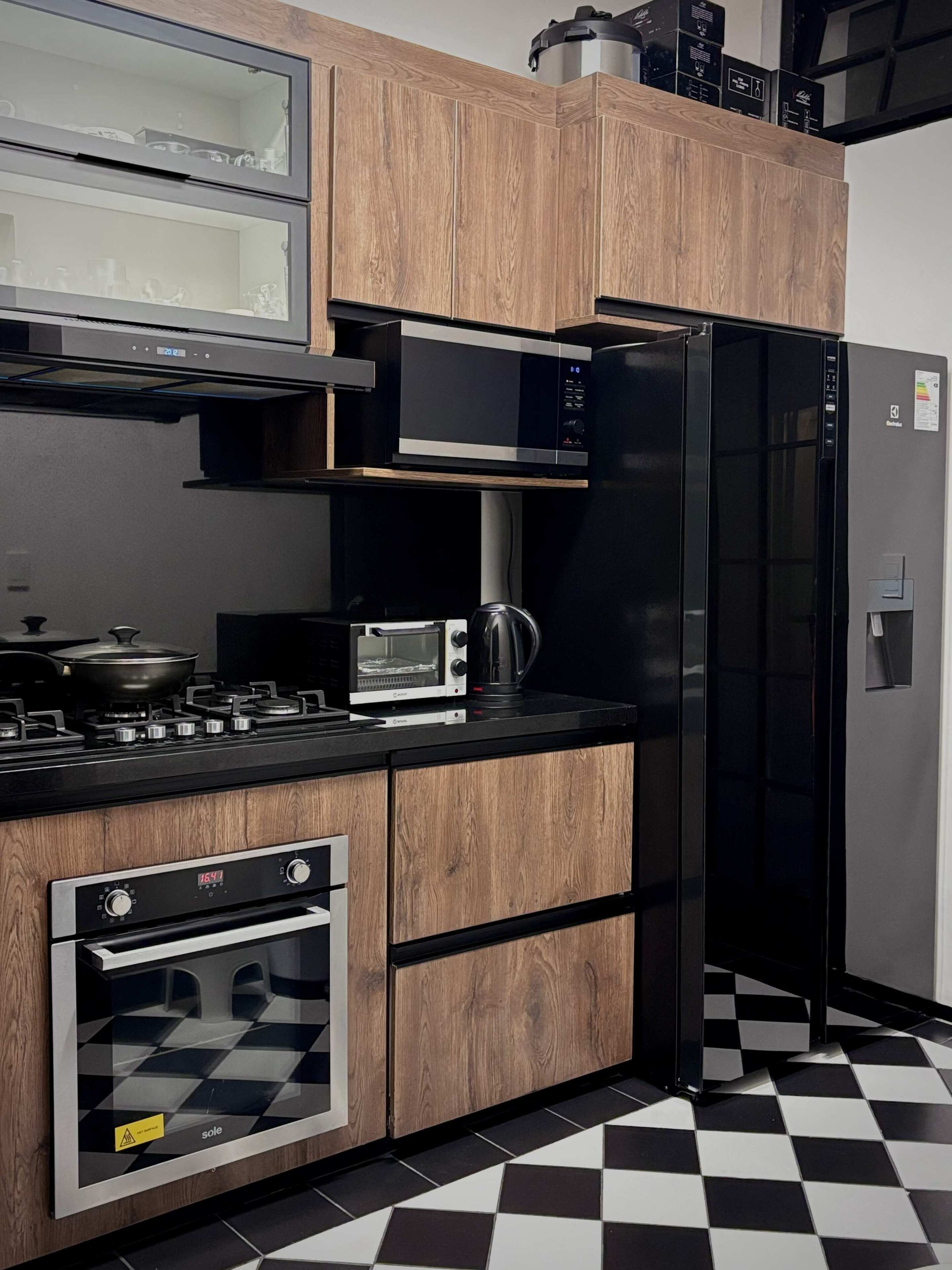 A modern kitchen with wood cabinetry, a microwave, a black refrigerator, a stove, and a checkered floor.