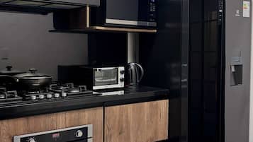 A modern kitchen with wood cabinetry, a microwave, a black refrigerator, a stove, and a checkered floor.