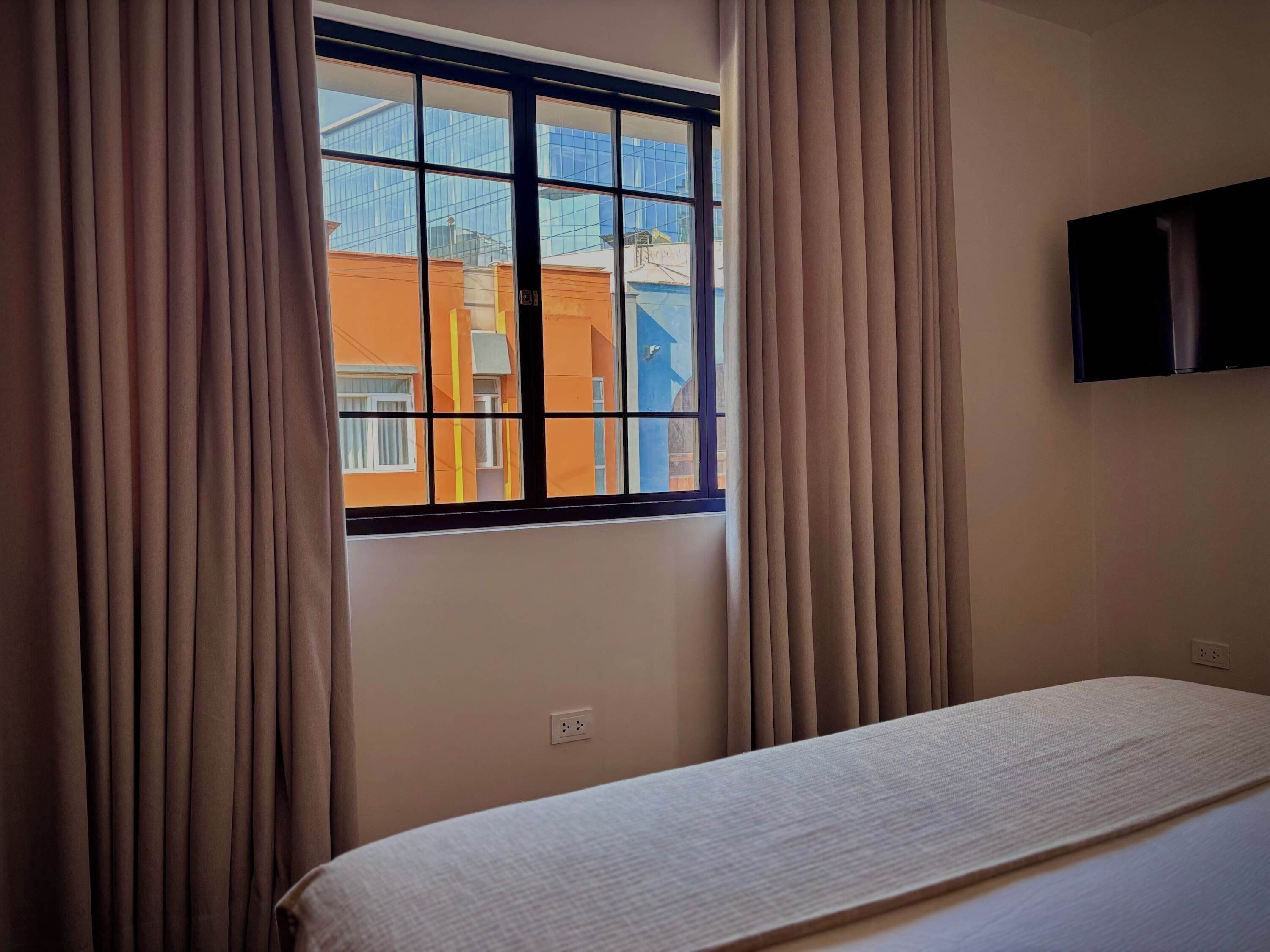 A room with a bed, a window with curtains, and a wall-mounted television.