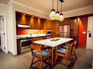 Une cuisine moderne avec des meubles en bois, un réfrigérateur en acier inoxydable et un coin repas comprenant une table et des chaises blanches.