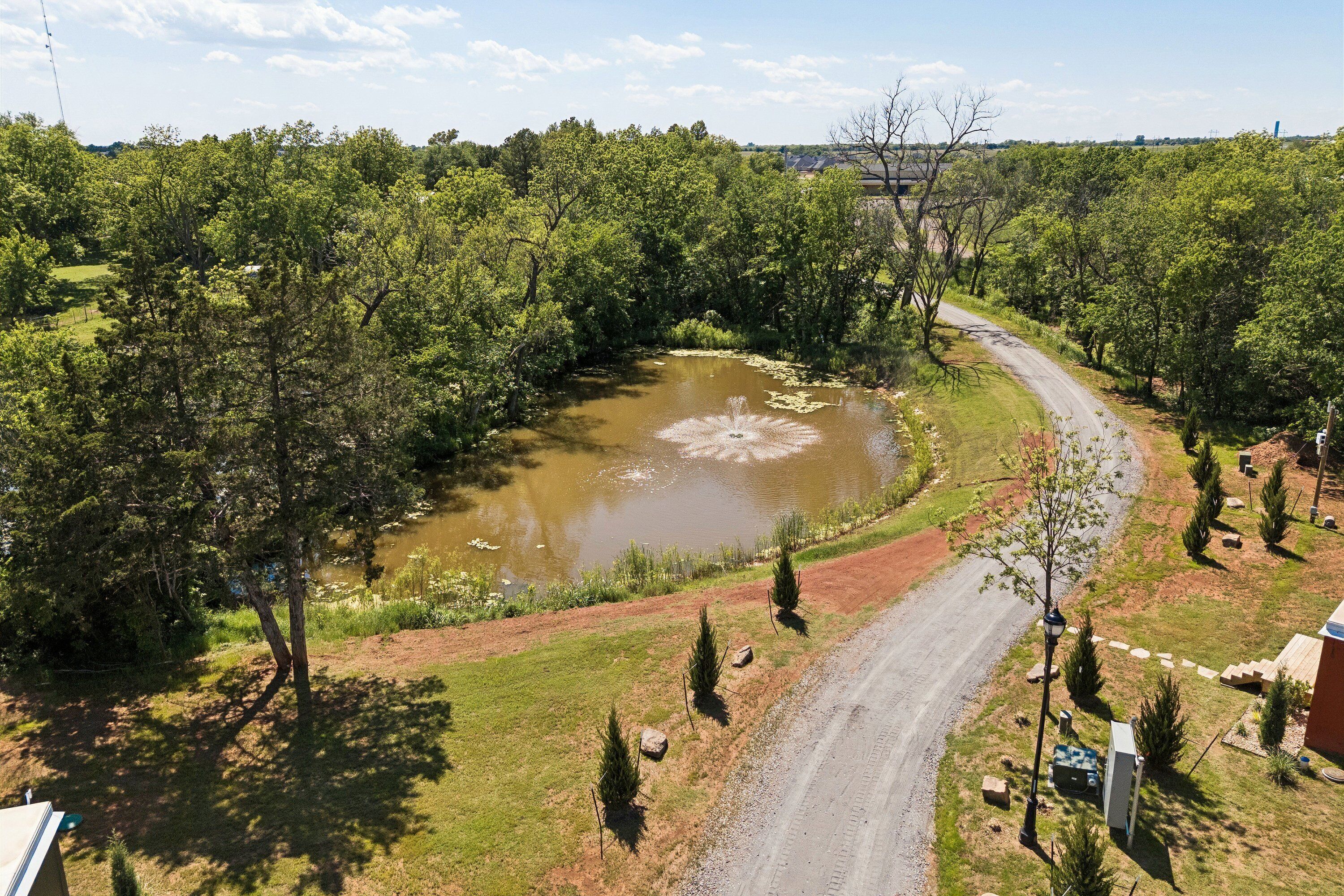 Ländliche Landschaft mit einer gewundenen Straße, einem Teich und verschiedenen Bäumen.