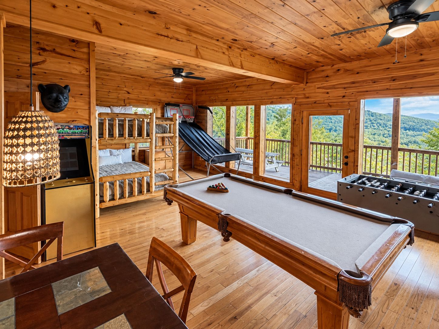 A wooden cabin interior with a pool table, a foosball table, a bunk bed, and a slide.