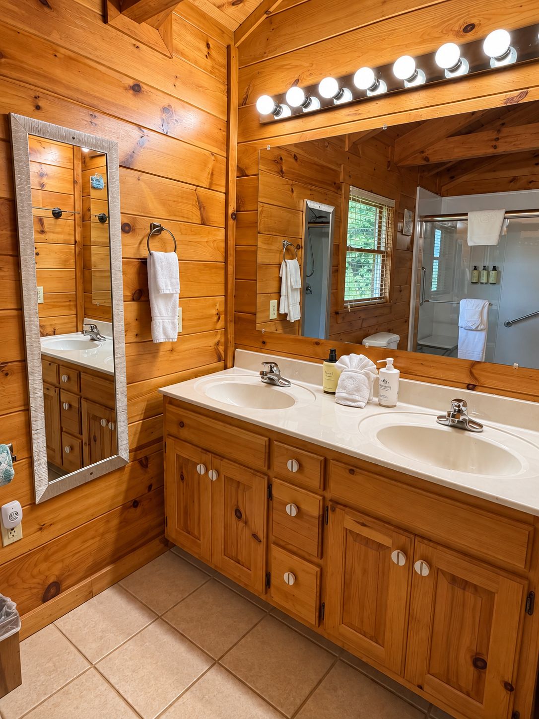 Bagno di una baita in legno con due lavandini, uno specchio grande e un mobile bagno con pensili.