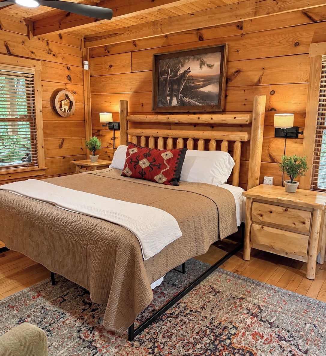 Una habitación tipo cabaña de madera con una cama, dos mesitas de noche, un paralelo, una lámpara de pared, un cuadro enmarcado y una ventana con persianas.