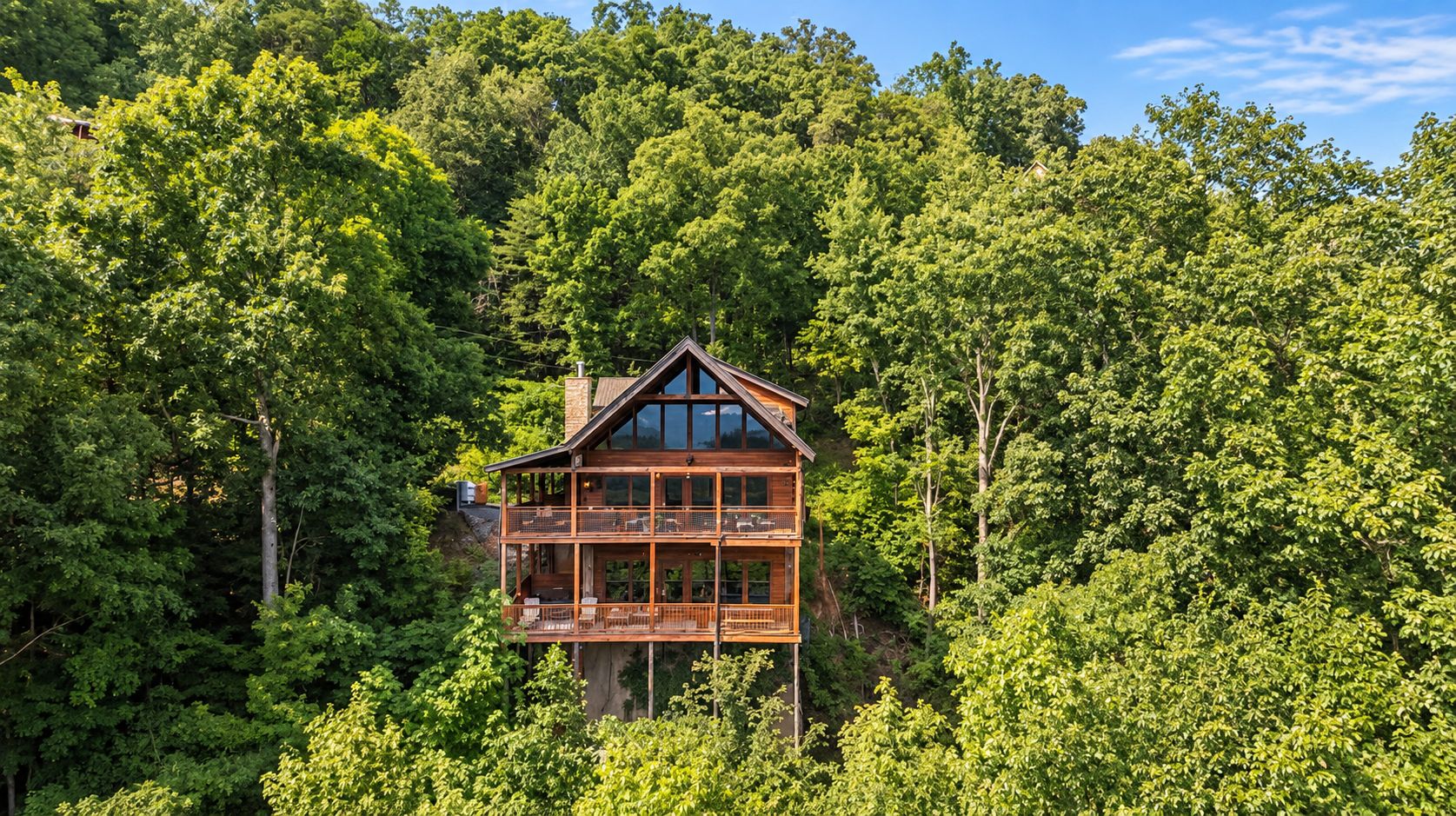 Een houten vakantiehuis met meerdere verdiepingen en een balkon, omgeven door dicht bos.