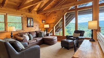 Een gezellig chalet interieur met een hoekbank, een kleine tafel en uitzicht op het bos door grote ramen.